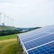 Wind turbines and a solar panel array in a German landscape under an overcast sky, with distant hydro and biomass installations in the background.