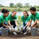 Volunteers planting a sapling and picking up litter along a riverbank in a clean, green outdoor setting.