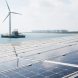Coastal renewable energy scene with solar panels in the foreground and a floating offshore wind turbine over calm water, with battery storage units suggested near the horizon.