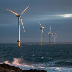 Offshore wind turbines on the U.S. East Coast at dusk, viewed from the shoreline with choppy water in the foreground.