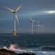 Offshore wind turbines on the U.S. East Coast at dusk, viewed from the shoreline with choppy water in the foreground.