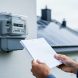 Close-up of a utility meter and a homeowner’s hands holding an unreadable electricity bill near solar panels, illustrating comparing energy costs.
