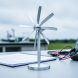 Close-up of a small wind turbine model on a lab table outdoors, with the rotor blades in sharp focus and other science tools softly blurred behind it.