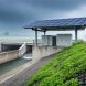 Solar microgrid and reinforced water and transportation infrastructure designed for climate resilience, captured in a stormy outdoor environment with rain mist in the distance.