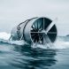 Offshore wave and tidal energy turbines mounted in ocean water under an overcast sky, showing waves and sea foam around the equipment.