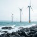 Offshore wind turbines generating clean power in the ocean near a rocky coastline under an overcast sky.